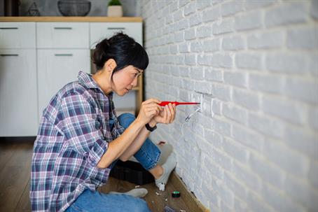 Focused woman sits on the floor doing a DIY wall socket installation